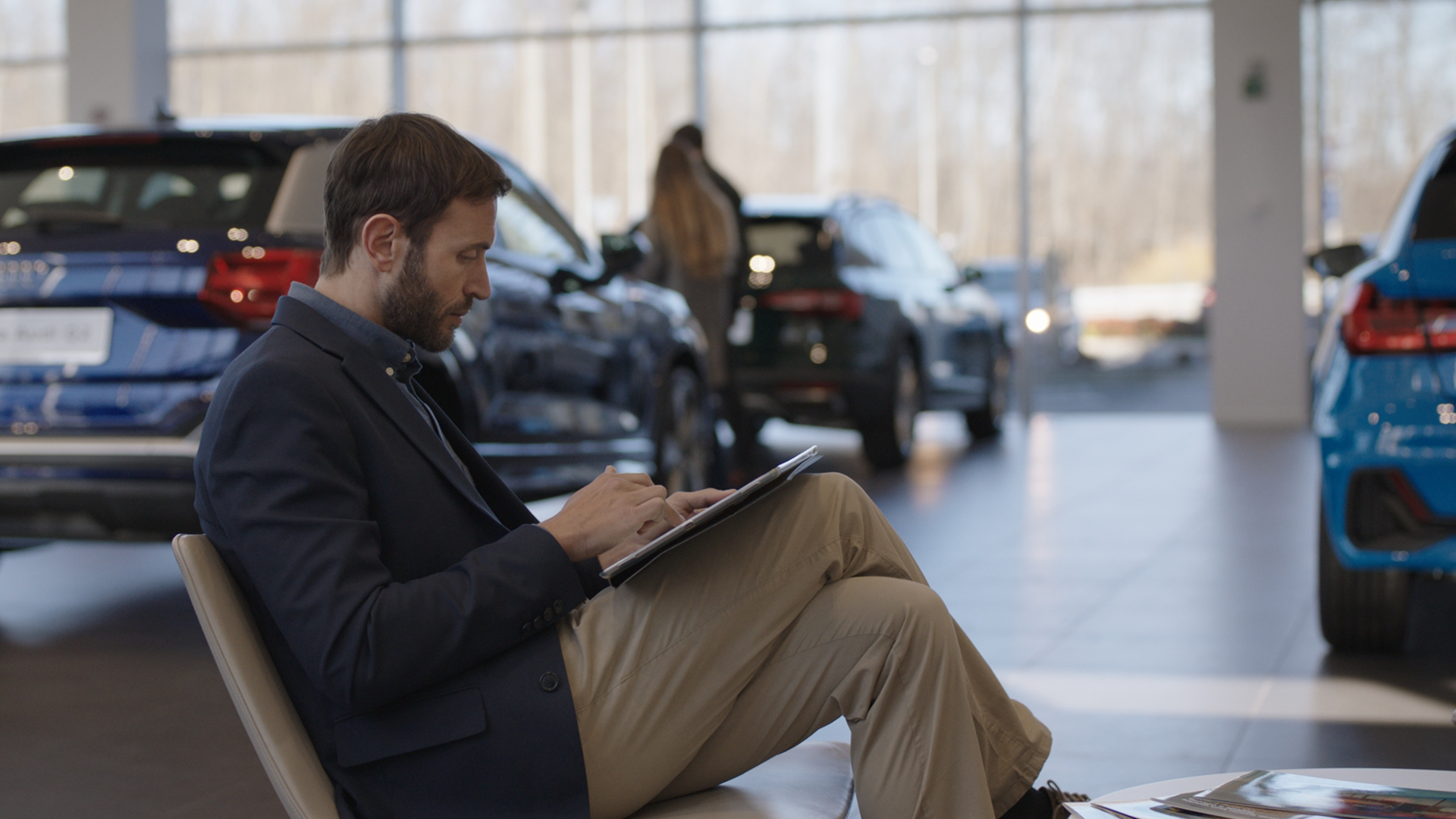 uomo seduto con tablet, presso un concessionario audi